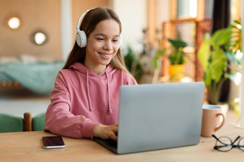 Niña con audífonos sonriendo frente a su laptop durante una clase de inglés online.